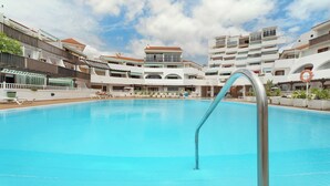 A swimming pool with a metal ladder, surrounded by multi-story buildings with balconies and a clear sky. - Gran Penthouse Luxury The 307 Parque Royal 1 Wiffi y Jacuzzi (Adeje)