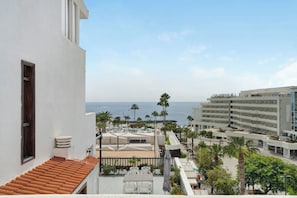 Hotel com terraço com vista para o mar, apresentando piscina, palmeiras e vista do oceano.