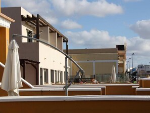 Een terras op het dak met buitenmeubilair en uitzicht op een gebouw met veel ramen.
