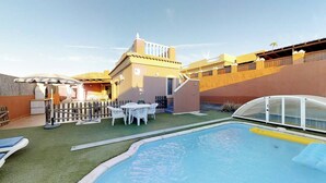 Un área de piscina con un pequeño patio, una zona de estar cubierta y una escalera que lleva a un nivel superior.