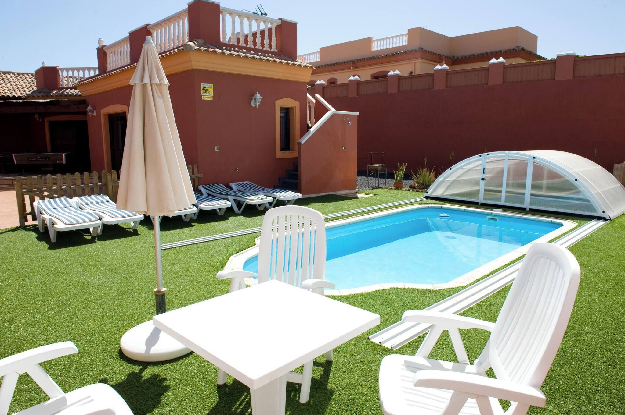Una piscina con sillones de descanso y una mesa, rodeada de césped artificial.