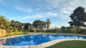 Μια πισίνα με περιμετρικό τοίχωμα από πέτρα, που περιβάλλεται από γρασίδι και δέντρα.