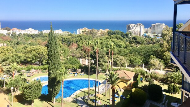 Μια θέα ενός θέρετρου με μια πισίνα, πλούσια βλάστηση και μια καθαρή, γαλάζια θάλασσα στο βάθος.