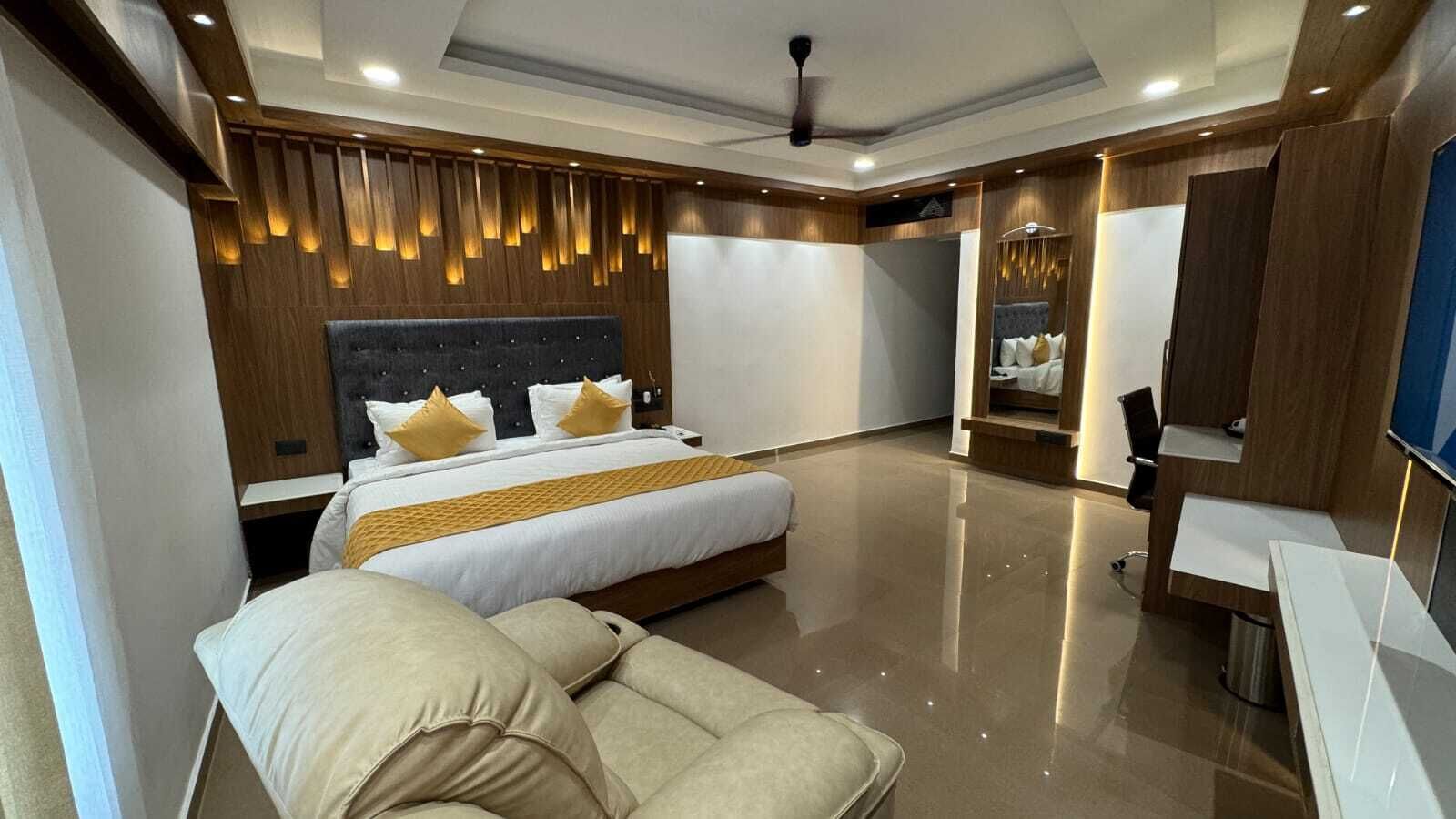 A modern hotel room with a large bed, a sofa, a desk, and a TV.