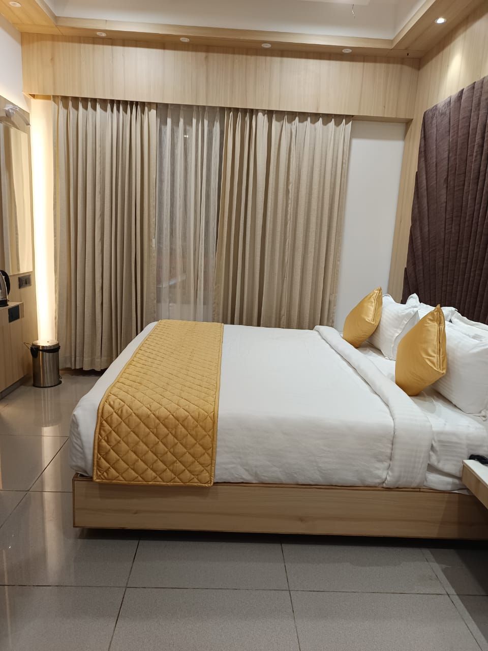 A hotel room with a large bed, a bedside table, and a curtain-covered window.