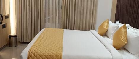 A hotel room with a large bed, a bedside table, and a curtain-covered window.
