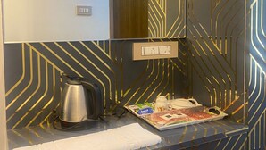 A modern bathroom with a geometric patterned wall, a towel, a kettle, and a tray with toiletries. - Hotel Royal stay (Thanjavur)