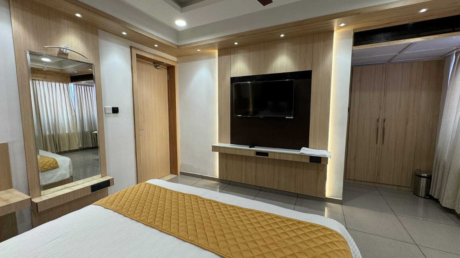 Una habitación de hotel moderna con una cama grande, un televisor de pantalla plana en la pared, paneles de madera y un espejo.