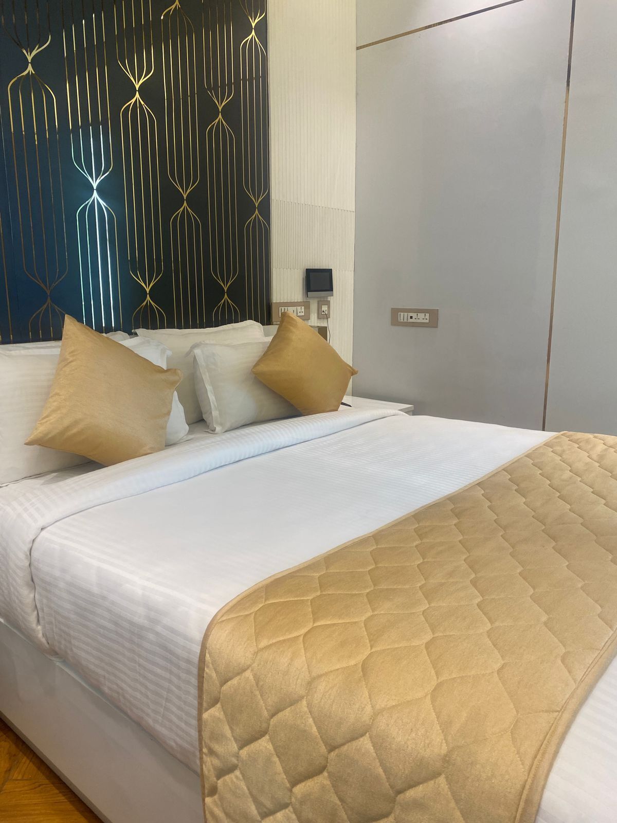 A neatly made bed with white linens and two beige pillows, a quilted beige throw blanket, and a wall with a geometric pattern.