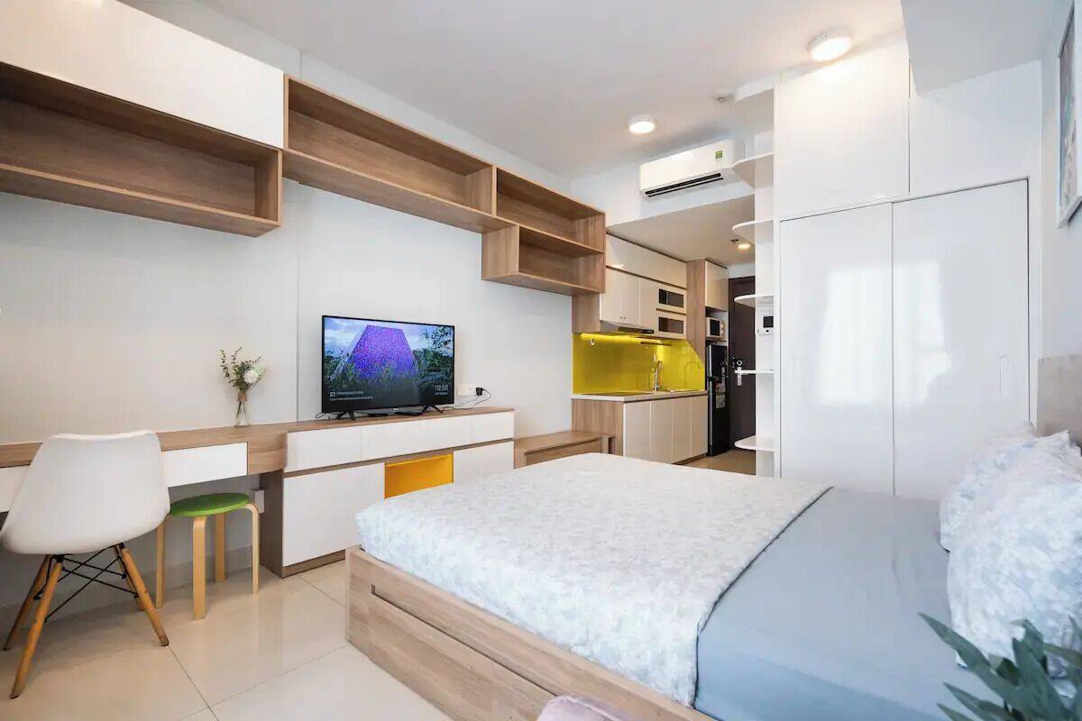 Una habitación de hotel moderna con una cama, un escritorio con computadora, un televisor y estantes empotrados.