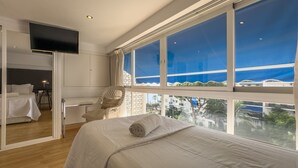 Un dormitorio con un ventanal grande, una cama, un televisor y una silla.