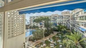 Un hotel de varios pisos con balcones, piscina y un jardín ajardinado con tumbonas.