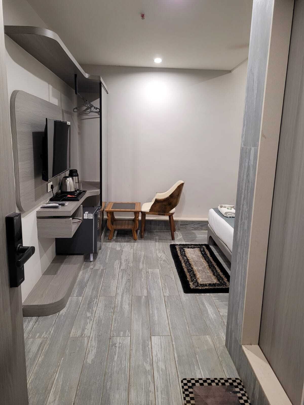 Ein kompaktes Hotelzimmer mit modernem Design, inklusive Flachbildfernseher, kleinem Schreibtisch mit Kaffeemaschine, Stuhl, Bett und Teppich mit Schachbrettmuster.