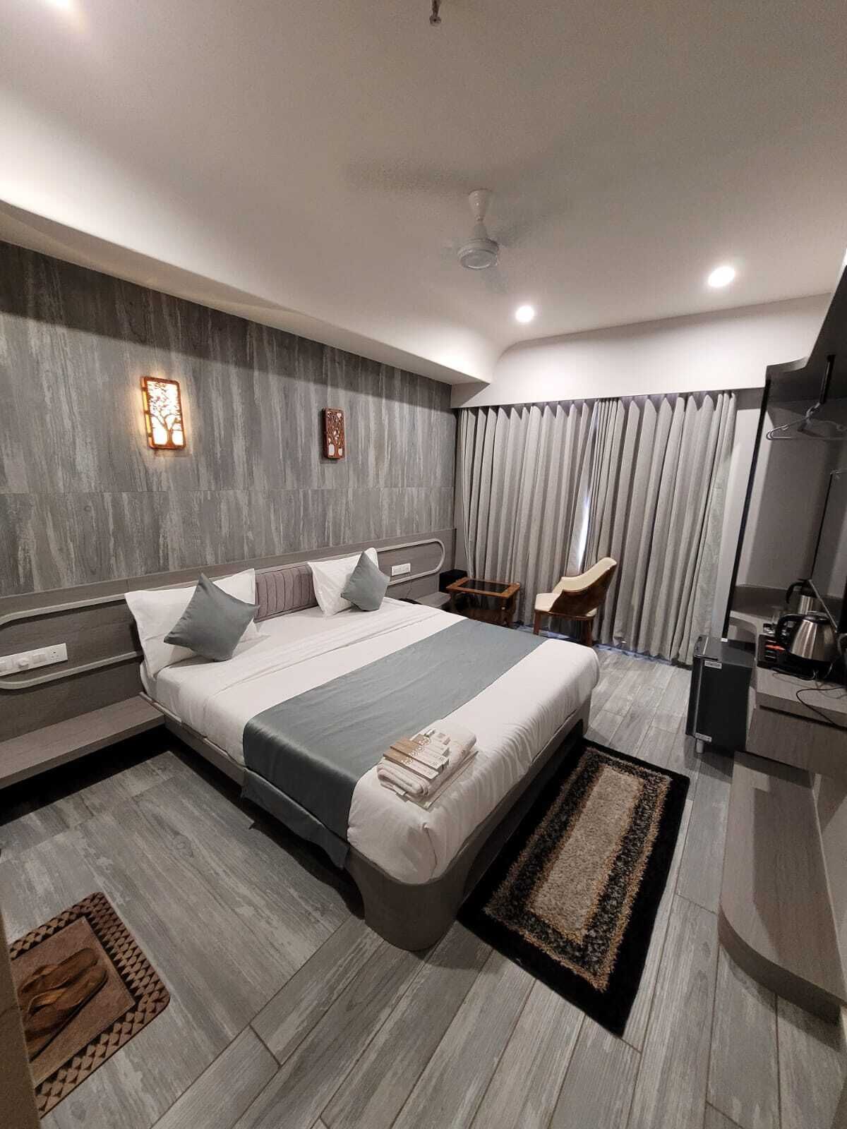 A modern hotel room with a large bed, a bedside table, a desk, and a chair.