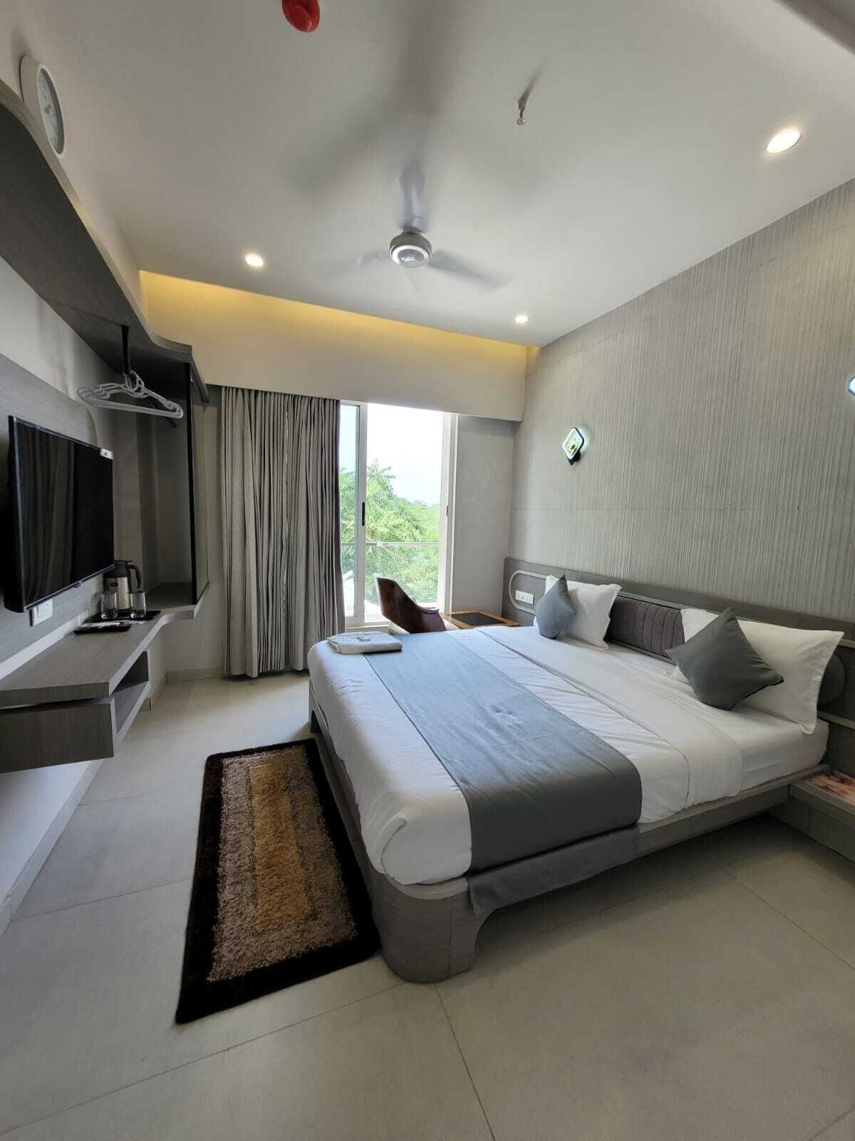 A modern hotel room with a large bed, a flat-screen TV, a desk, and a large window with curtains.
