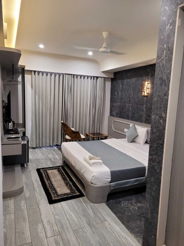 A modern hotel room with a large bed, a desk with a chair, a small table, and a ceiling fan. - The Royal Era Hotel (Gandhinagar)