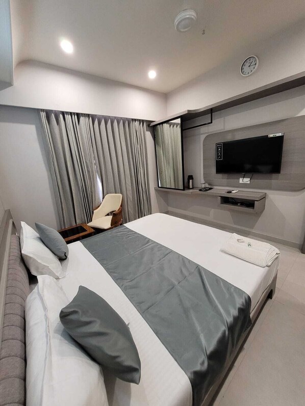 A modern hotel room with a large bed, a TV mounted on the wall, and a seating area with a chair and curtains. - The Royal Era Hotel (Gandhinagar)