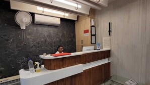 Ein moderner Empfangstresen mit Holzoptik, eine Wand aus schwarzem Marmor und ein Glastisch mit Zeitungen.