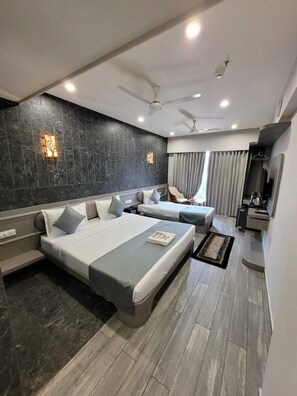A modern hotel room with two beds, a seating area, a TV, and a ceiling fan. - The Royal Era Hotel (Gandhinagar)