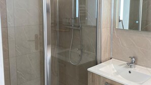 Une salle de bain moderne avec une douche à parois de verre, un lavabo blanc et un meuble-lavabo en bois.