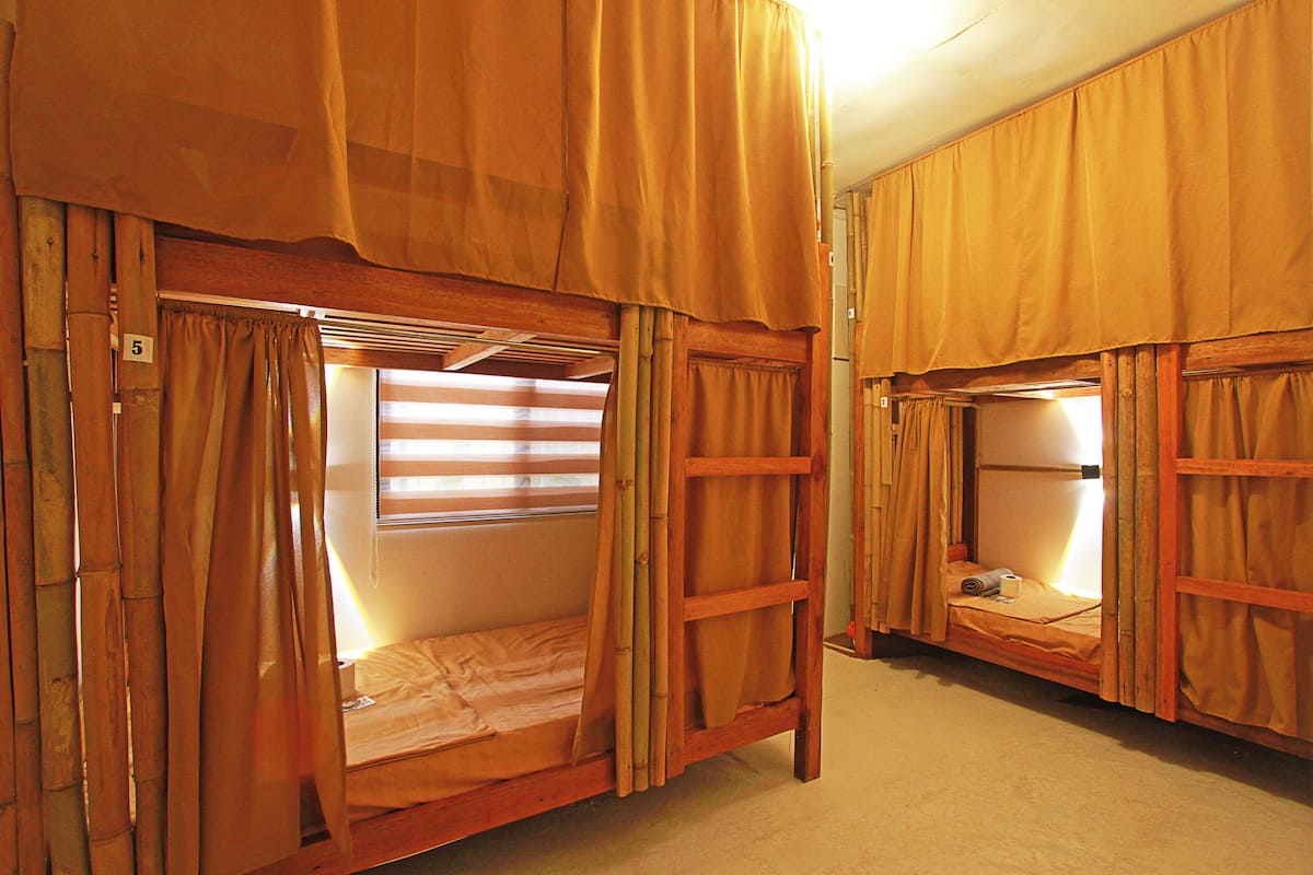 Zwei Stockbetten mit Vorhängen, ein Fenster mit Jalousien und eine Holzleiter.