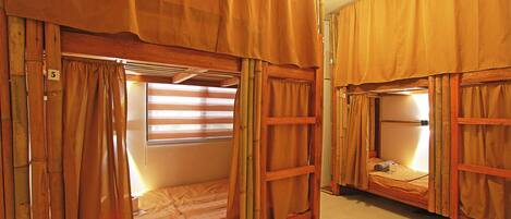 Two bunk beds with curtains, a window with blinds, and a wooden ladder.