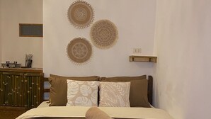A neatly made bed with a brown bedspread and pillows, a pair of rolled towels, and three wall-mounted decorative plates. - Yellow Banana Siargao (General Luna)
