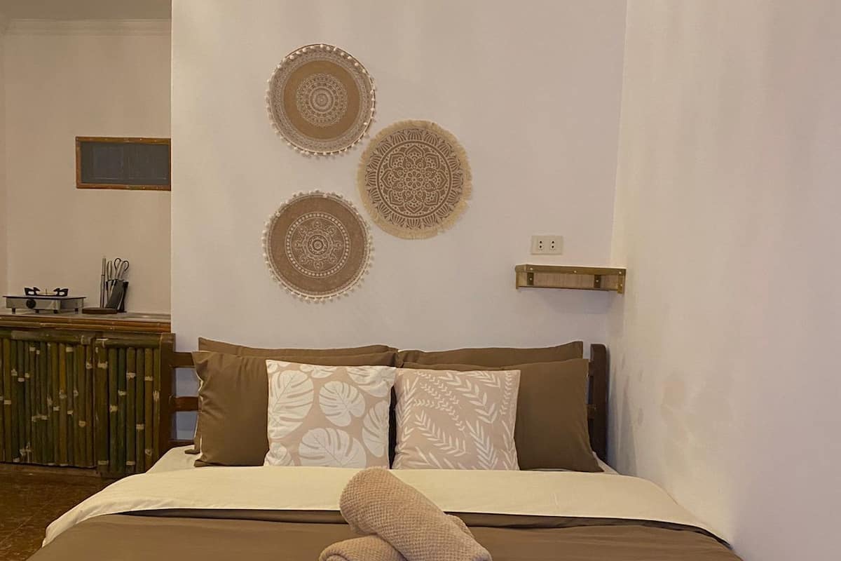 Ein ordentlich bezogenes Bett mit brauner Tagesdecke und Kissen, ein Paar zusammengerollte Handtücher und drei dekorative Wandteller.