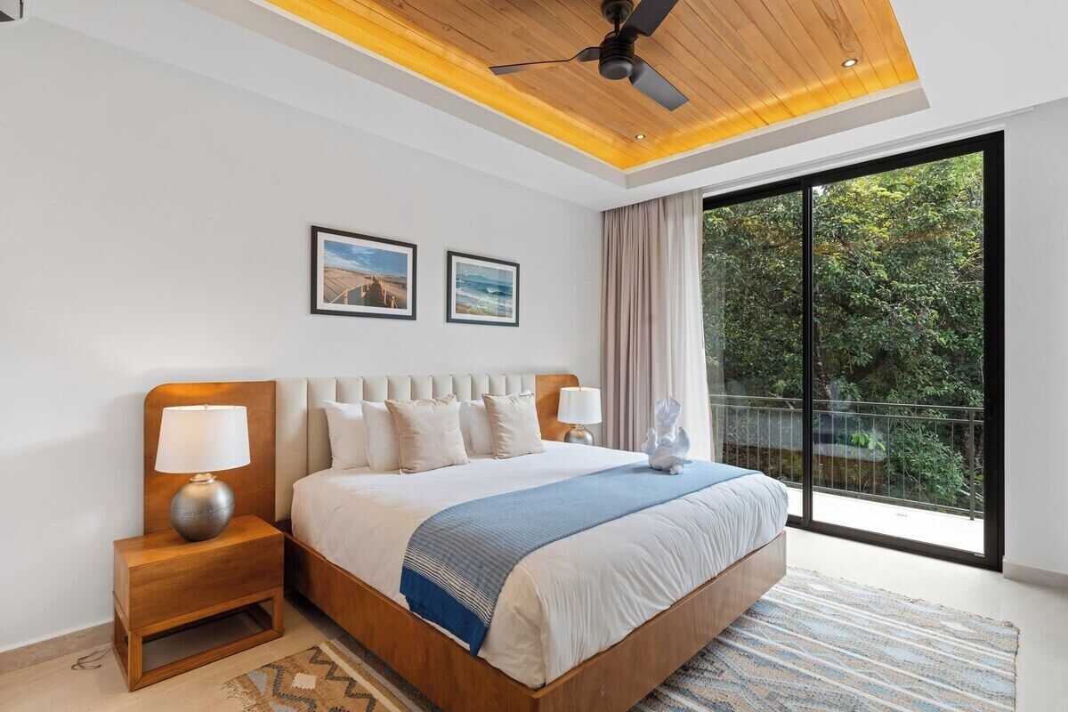 A modern hotel room with a large bed, a ceiling fan, and a view of the outdoors through a sliding glass door.