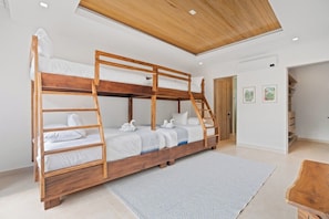 A bunk bed with a wooden frame, white bedding, and a ladder. There is a white rug on the floor, and a wooden coffee table to the right.