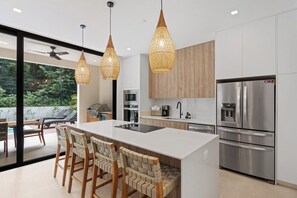 Una cocina moderna con una isla central, electrodomésticos de acero inoxidable e iluminación colgante de mimbre.