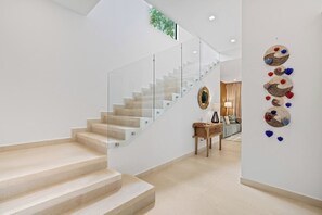A modern interior with a glass staircase, a wall-mounted art piece, and a wooden table with a vase.