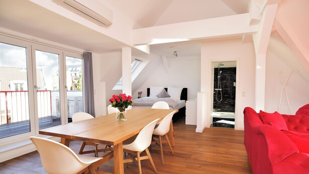 Un interior moderno con una mesa de comedor de madera, sillas blancas, un sofá rojo y una cama con tragaluz.