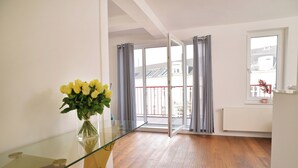 Una habitación con una mesa de vidrio, un jarrón de flores amarillas, suelo de madera y una puerta corrediza de cristal que da a un balcón.