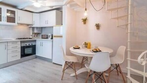A modern kitchen with white cabinets, a dining table with chairs, and a hanging light fixture. - Duplex Lx Factory 2 BR - Patio - Free parking (Lisbon)