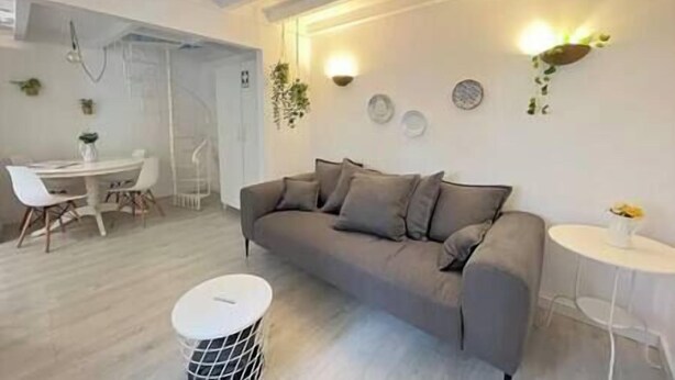 A modern living room with a grey sofa, a round coffee table, and a dining area with a white table and chairs. - Duplex Lx Factory 2 BR - Patio - Free parking (Lisbon)
