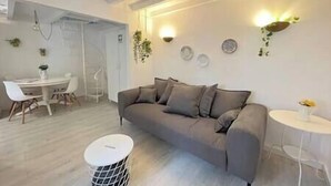A modern living room with a grey sofa, a round coffee table, and a dining area with a white table and chairs.