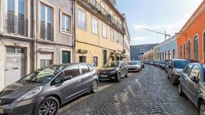 A cobblestone street lined with parked cars and buildings with multiple stories and balconies. - Duplex Lx Factory 2 BR - Patio - Free parking (Lisbon)