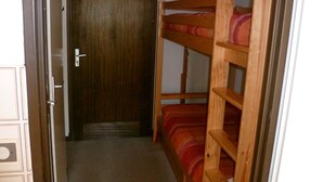 A narrow hallway leading to a wooden door, with a bunk bed on the right. - Cozy T2 near slopes with parking and balcony (Le Lioran)