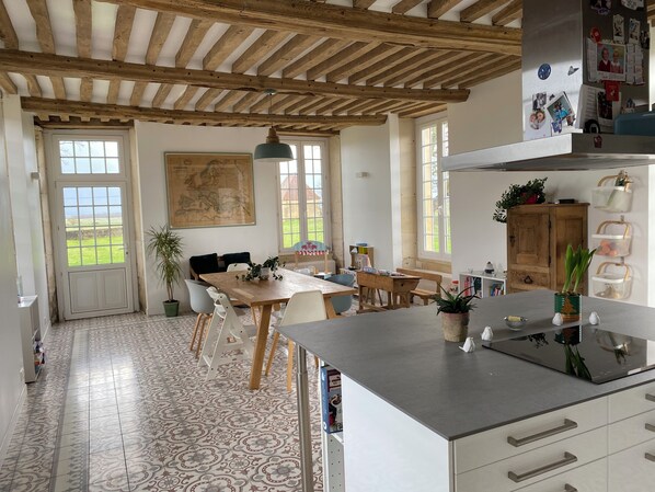 A spacious kitchen with a wooden ceiling, a dining area with a table and chairs, and a view of the outdoors through large windows.