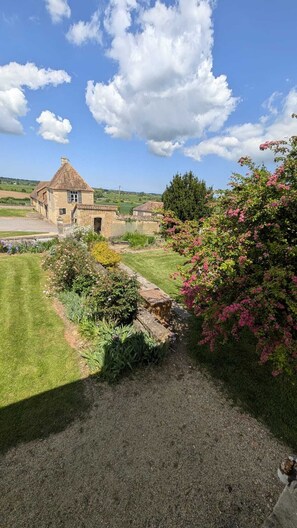 A stone building with a sloped roof, surrounded by a well-maintained garden with various plants and flowers.