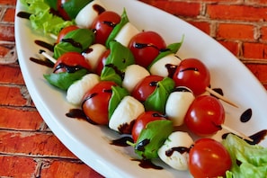 A plate of mozzarella and cherry tomatoes on skewers with basil leaves and a drizzle of balsamic glaze. - Casa Amabile With Pool (Leggiuno)