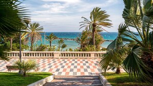 Une terrasse à carreaux offrant une vue sur la mer, des palmiers et un lampadaire.