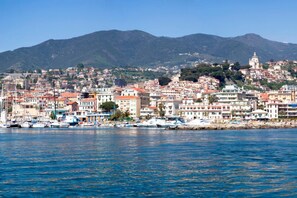 A coastal cityscape with a marina, buildings, and a mountain backdrop. - La Finestra Sul Giardino (Sanremo)