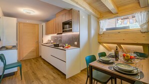 Una cocina compacta con armarios de madera, horno integrado y comedor con mesa lista para dos.