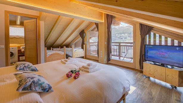 Un dormitorio de cabaña de madera acogedor con una cama grande, un televisor y un balcón con vistas a las montañas.
