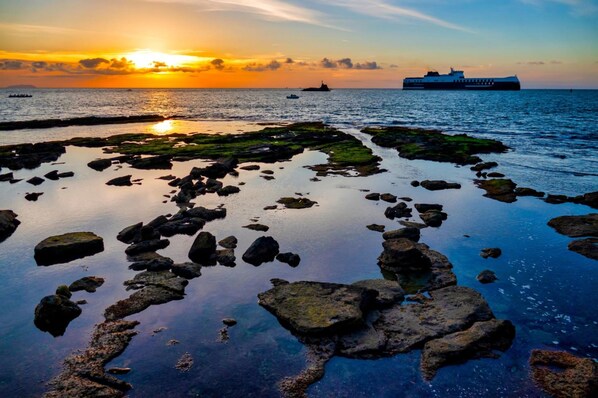 A coastal scene with a sunset, rocky shoreline, and a large ship in the distance. - Ardenza s Aires 600 Mt From Sea (Livorno)