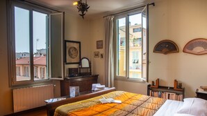 A hotel room with a bed, a dresser, a mirror, and a window with a view of buildings. - Casa Lucia in San Remo (Sanremo)