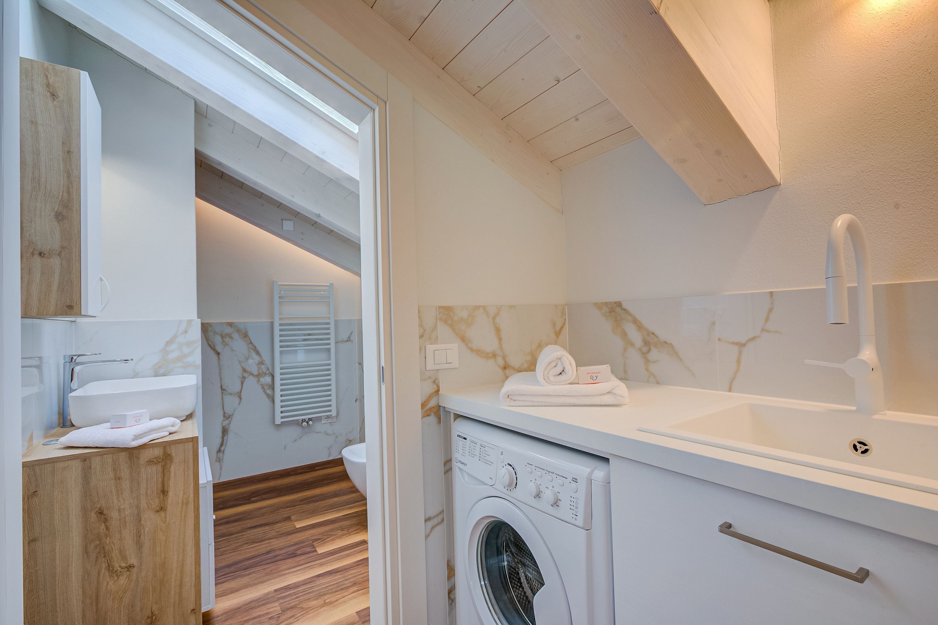 Une salle de bain moderne équipée d’un lave-linge intégré, d’un évier et d’un meuble en bois.