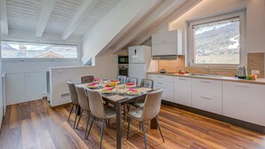 A modern kitchen with a dining area, featuring a wooden ceiling, white cabinets, and a large window with a view of a mountainous landscape. - Cimetta in Livigno With 3 Bedrooms and 2 Bathrooms (Livigno)